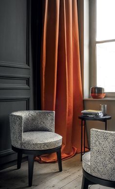 two chairs sitting next to each other in front of a window with orange drapes