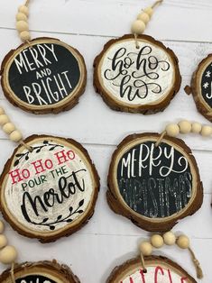 christmas ornaments made out of wood and decorated with hand painted words on them, hanging from strings