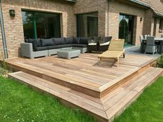 a large wooden deck in front of a brick building with furniture on the grass outside