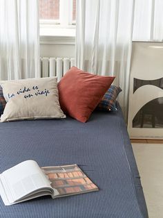 a bed with pillows and a book on it in front of a white curtained window