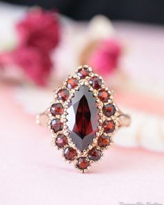 a red stone ring sitting on top of a pink flowered tablecloth with roses in the background