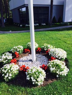 a clock made out of flowers in the middle of a lawn with a flag pole