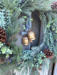 a wreath with bells hanging from it and pine cones on the front, surrounded by greenery