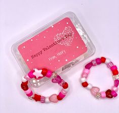 two pink and red bracelets sitting next to each other on a white surface with a happy valentine's day card in the background