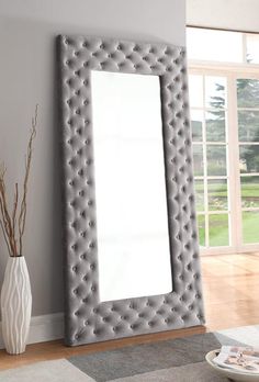 a large gray mirror sitting on top of a wooden floor next to a white vase