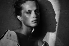 a black and white photo of a woman leaning against a wall with her head turned to the side