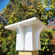 a white box sitting on top of a wooden post in front of some trees and bushes