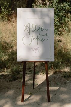 a sign that is sitting on top of a wooden easel in the dirt near some grass