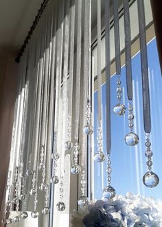 a window with glass beads hanging from it's side and flowers in the foreground