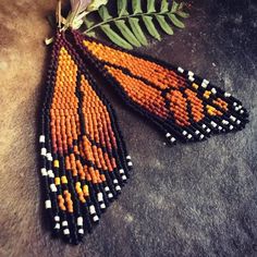 a pair of orange and black beaded earrings with green leaves on the top one