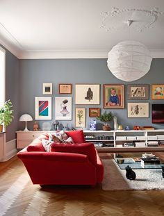 a living room with red couches and pictures on the wall above it, in front of a white chandelier