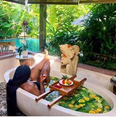 a woman sitting in a bathtub with an elephant statue next to it and fruit on the tray