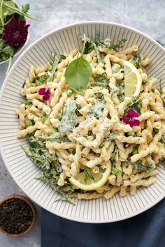 a white bowl filled with pasta salad and garnished with lemon wedges on top