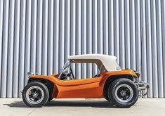 an orange and white dune buggy parked in front of a metal building with corrugated walls