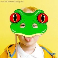 a young boy wearing a green frog mask with red eyes and tongue sticking out his tongue