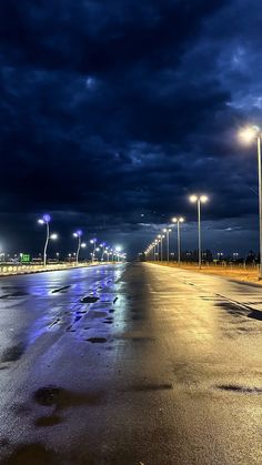 an empty street at night with the lights on and dark clouds in the sky above