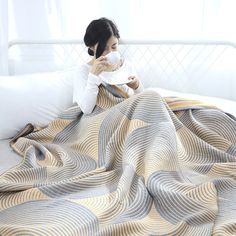 a woman sitting on a bed covering her face with a blanket