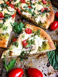 two slices of pizza with tomatoes, cheese and basil on a baking sheet next to cherry tomatoes