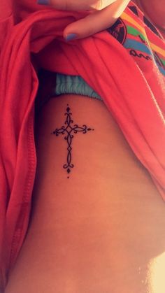 a cross tattoo on the back of a woman's stomach is shown in this image