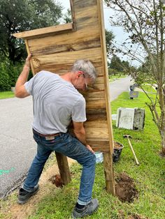 a man leaning against a wooden sign in the grass with his head on top of it