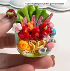 a hand holding a small ring with many different things in the bowl on top of it