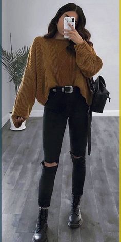 a woman taking a selfie with her cell phone and wearing black ripped jeans, a brown sweater and boots