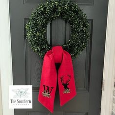 a christmas wreath on the front door with a red scarf hanging from it's side