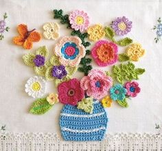 crocheted flowers in a blue vase on a white tablecloth with lace border