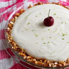 a cake with white frosting and a cherry on top is sitting on a pink checkered tablecloth