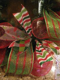 a christmas wreath on top of a tree with red, green and white striped ribbon