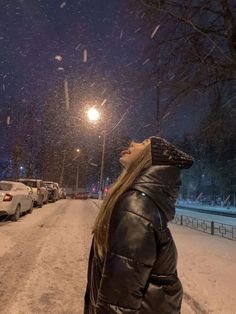 a woman standing in the middle of a snowy street at night with her eyes closed