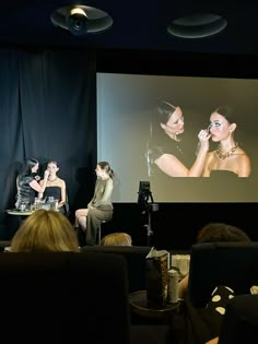 three women sitting in front of a projector screen while one woman talks on the phone