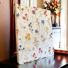 a table with a flowered cloth on it and a vase full of flowers in the background