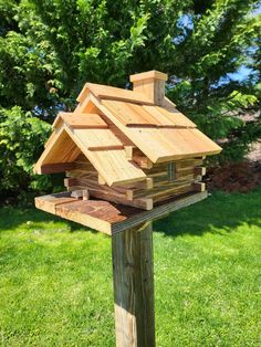 a wooden bird house sitting on top of a post in front of some grass and trees