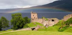 an old castle with a rainbow in the sky above it and water on the other side