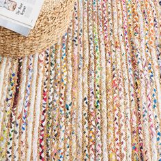 a basket with a book sitting on top of it next to a rug covered in multicolored yarn