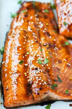 two salmon fillets with sesame seeds and parsley on top in a white dish