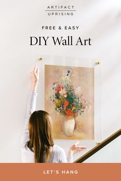 a woman pointing at a painting on the wall with text overlay that reads, let's hang