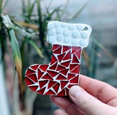 a hand holding up a red and white christmas stocking ornament with holes in it