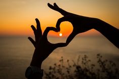 two hands making a heart shape with the sun setting in the background