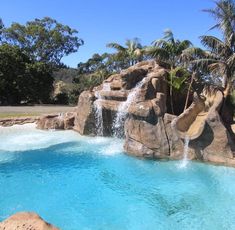 a large pool with waterfall and rock formations in the middle, surrounded by palm trees