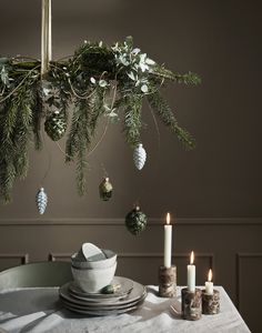 a dining room table set for christmas with candles and ornaments hanging from the chandelier