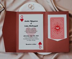 a red and white wedding card on top of a table next to a pair of rings