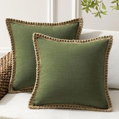 two green pillows sitting on top of a white couch next to a wicker basket