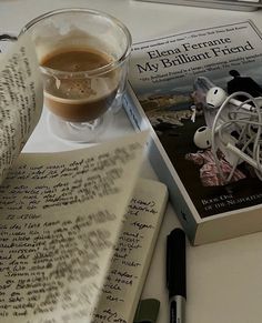 a cup of coffee next to an open book with writing on it and a pen