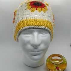 a knitted hat with yellow and red flowers on it next to a glass ring