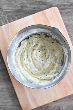 a metal bowl filled with white sauce on top of a wooden cutting board