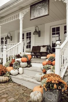 pumpkins and gourds line the front steps of a white house with porch railing