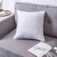 a white pillow sitting on top of a gray couch next to a book and eyeglasses