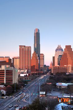 the city skyline is lit up at sunset with tall buildings in the background and cars driving on the road